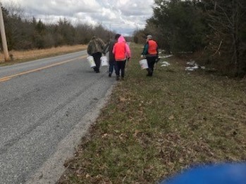 Three people walking down the street away from the camera with white buckets in their hands